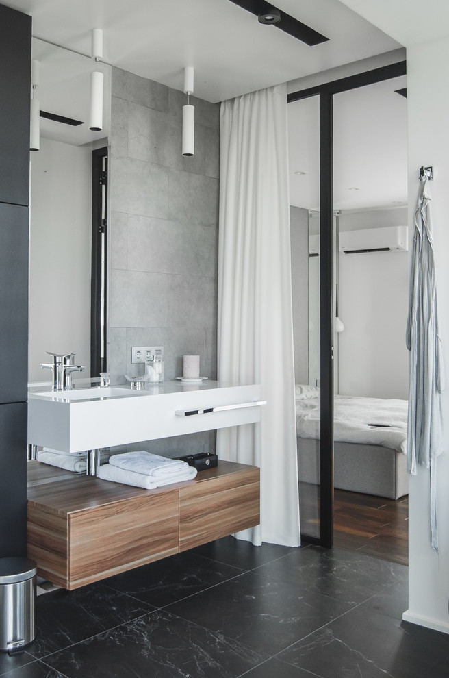 This is an example of a contemporary bathroom in Other with flat-panel cabinets, medium wood cabinets, gray tile, black floor, white benchtops and an integrated sink.
