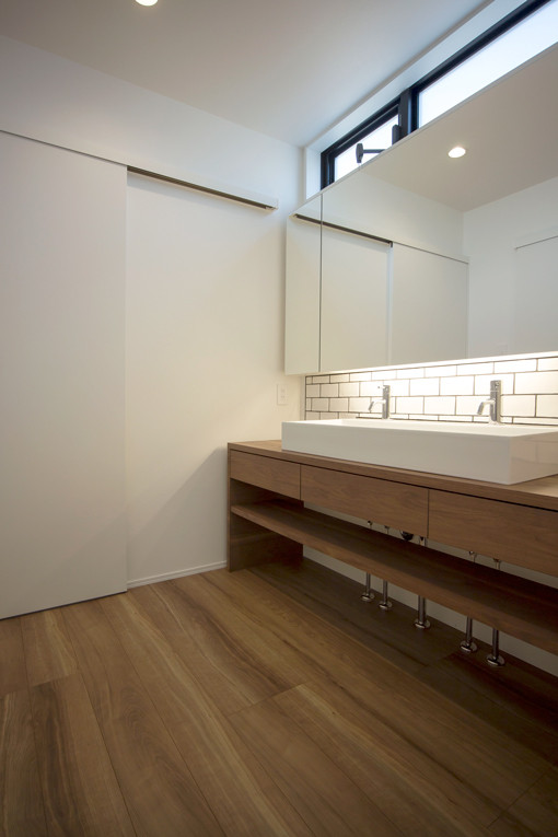 Foto på ett litet funkis brun toalett, med möbel-liknande, vita skåp, vit kakel, porslinskakel, vita väggar, plywoodgolv, ett nedsänkt handfat och brunt golv