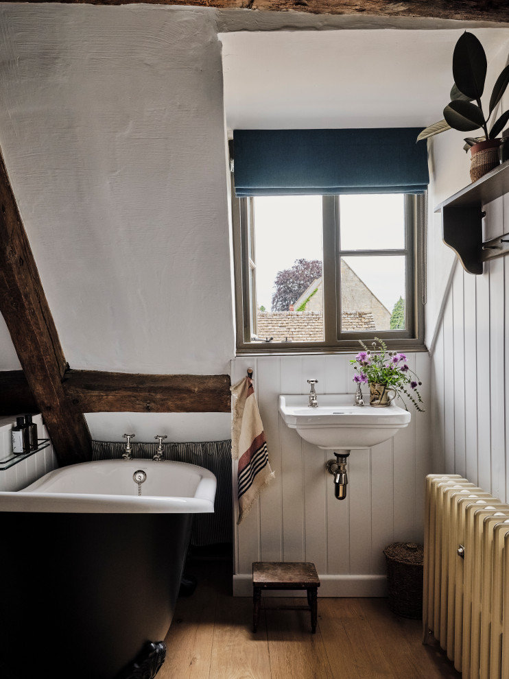 Mittelgroßes Landhaus Badezimmer mit Löwenfuß-Badewanne, weißer Wandfarbe, hellem Holzboden, Wandwaschbecken, WC-Raum, Einzelwaschbecken, schwebendem Waschtisch und freigelegten Dachbalken in Oxfordshire