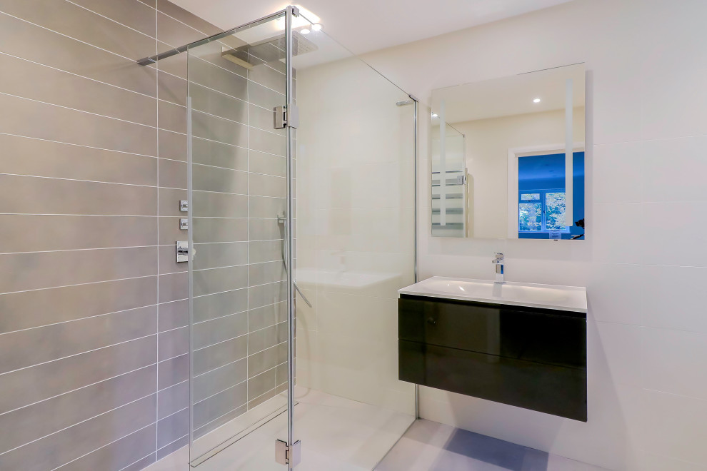 Design ideas for a mid-sized contemporary master wet room bathroom in Surrey with a wall-mount toilet, white walls, porcelain floors, a wall-mount sink, beige floor, porcelain tile, white benchtops, glass-front cabinets, black cabinets, beige tile, glass benchtops, an open shower, a single vanity and a floating vanity.