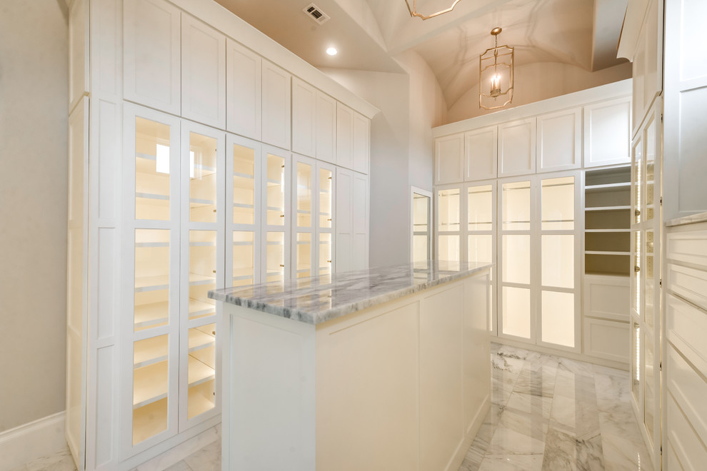Photo of a large gender-neutral walk-in wardrobe in Dallas with glass-front cabinets, white cabinets, marble floors and white floor.