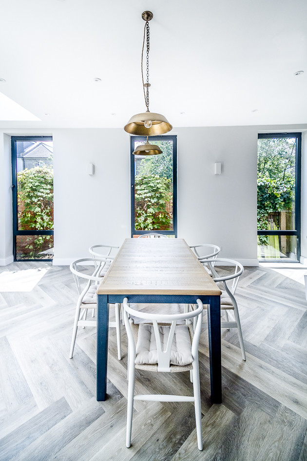 Large contemporary l-shaped open plan kitchen in Surrey with an undermount sink, shaker cabinets, blue cabinets, solid surface benchtops, white splashback, mosaic tile splashback, stainless steel appliances, medium hardwood floors, with island, grey floor and white benchtop.
