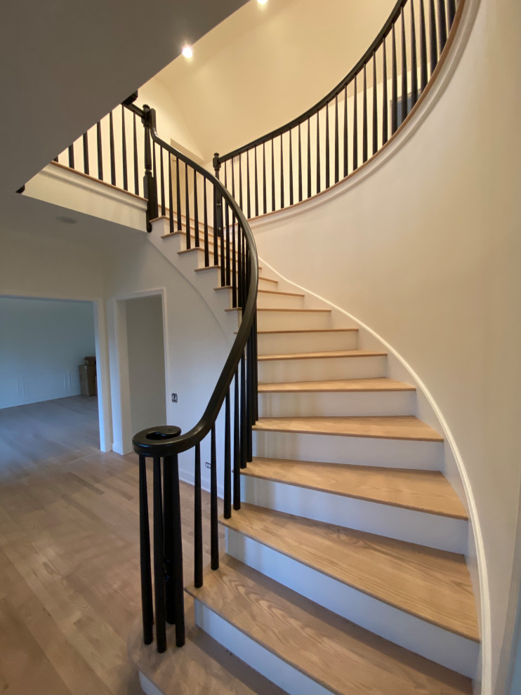Стильный дизайн: большая изогнутая лестница в стиле модернизм с деревянными ступенями, крашенными деревянными подступенками, деревянными перилами и деревянными стенами - последний тренд