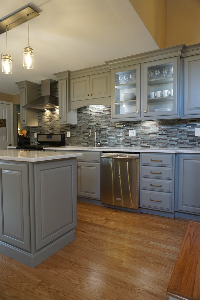 Inspiration for a small traditional l-shaped eat-in kitchen in Providence with a triple-bowl sink, raised-panel cabinets, grey cabinets, quartz benchtops, grey splashback, mosaic tile splashback, stainless steel appliances, medium hardwood floors, with island and white benchtop.