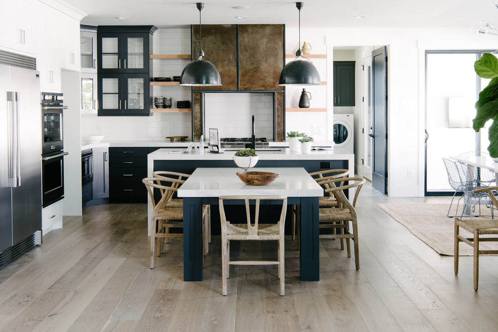 Photo of a large transitional l-shaped open plan kitchen in Salt Lake City with an undermount sink, recessed-panel cabinets, blue cabinets, white splashback, stainless steel appliances, light hardwood floors, with island and beige floor.