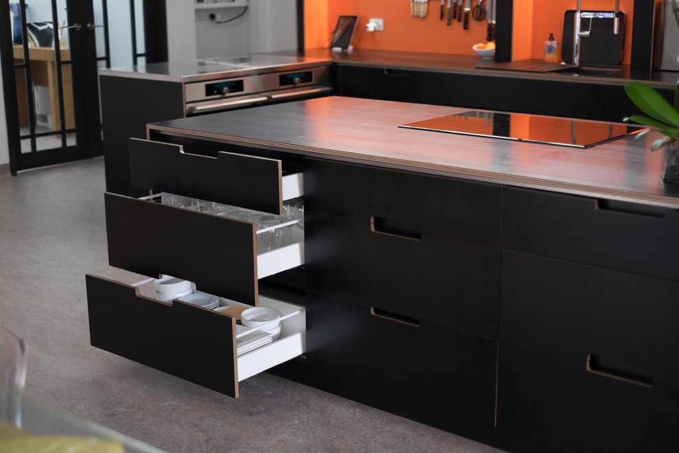 Photo of a large contemporary l-shaped open plan kitchen in Perth with a double-bowl sink, flat-panel cabinets, black cabinets, orange splashback, stainless steel appliances, linoleum floors, with island and black benchtop.
