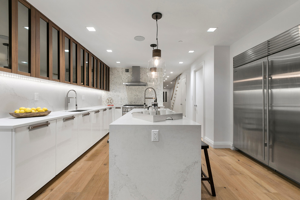 This is an example of a large contemporary l-shaped eat-in kitchen in New York with an undermount sink, glass-front cabinets, medium wood cabinets, marble benchtops, grey splashback, stainless steel appliances, light hardwood floors, with island and brown floor.