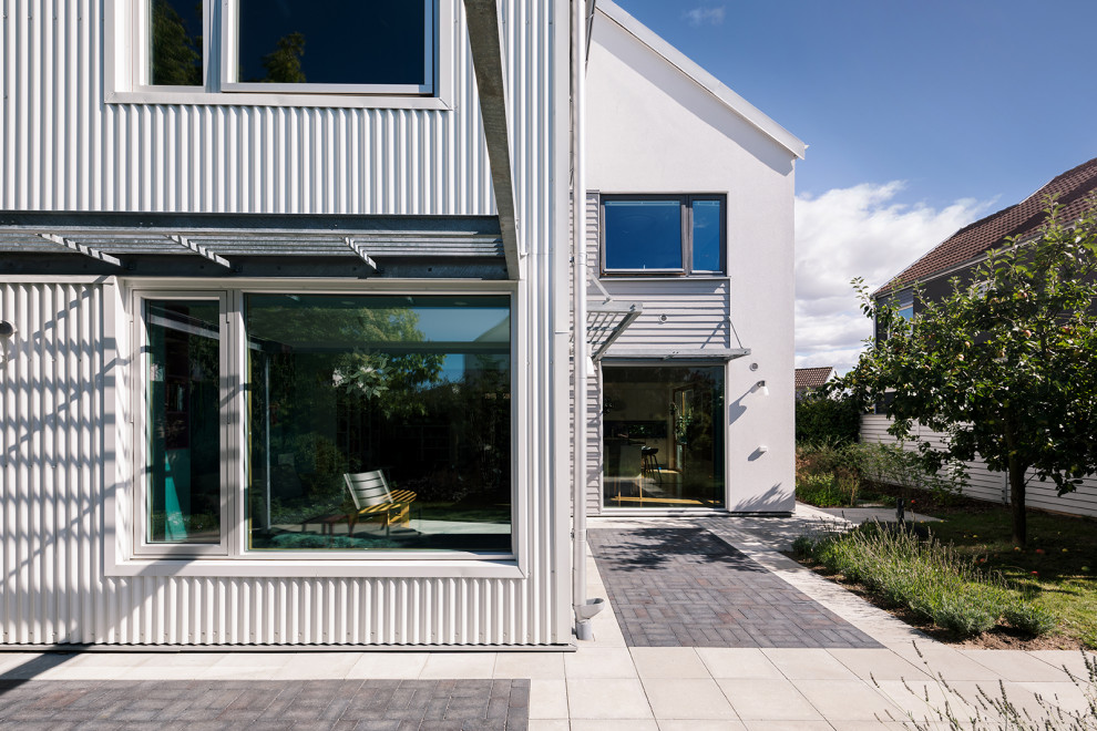 This is an example of a small and white modern two floor detached house in Malmo with metal cladding, a metal roof and a white roof.