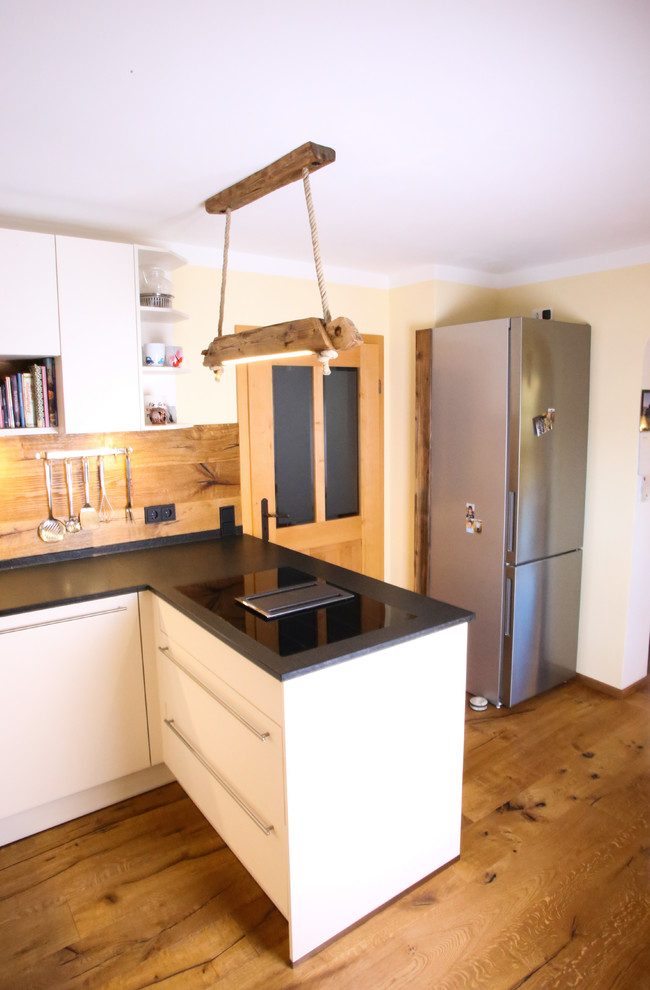 Küche ohne Insel in U-Form mit Unterbauwaschbecken, Kassettenfronten, Schränken im Used-Look, Granit-Arbeitsplatte, Küchenrückwand in Braun, Rückwand aus Holz, schwarzen Elektrogeräten, dunklem Holzboden, braunem Boden und schwarzer Arbeitsplatte in Munich