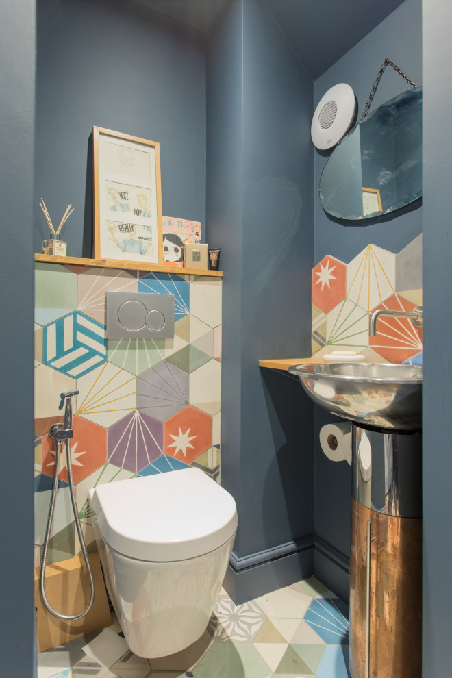 Inspiration for an industrial powder room in London with a wall-mount toilet, multi-coloured tile, blue walls, cement tiles, a drop-in sink, wood benchtops, multi-coloured floor and brown benchtops.