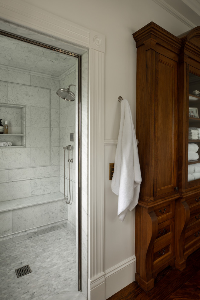 Klassisk inredning av ett stort vit vitt en-suite badrum, med luckor med profilerade fronter, vita skåp, ett fristående badkar, en dusch i en alkov, vita väggar, mörkt trägolv, ett integrerad handfat, marmorbänkskiva, brunt golv och dusch med gångjärnsdörr