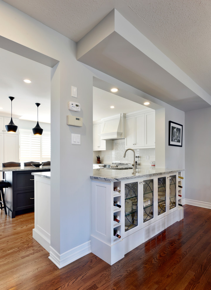 Open concept kitchen - large transitional u-shaped light wood floor and beige floor open concept kitchen idea in Ottawa with an undermount sink, shaker cabinets, white cabinets, granite countertops, white backsplash, subway tile backsplash, stainless steel appliances, an island and gray countertops