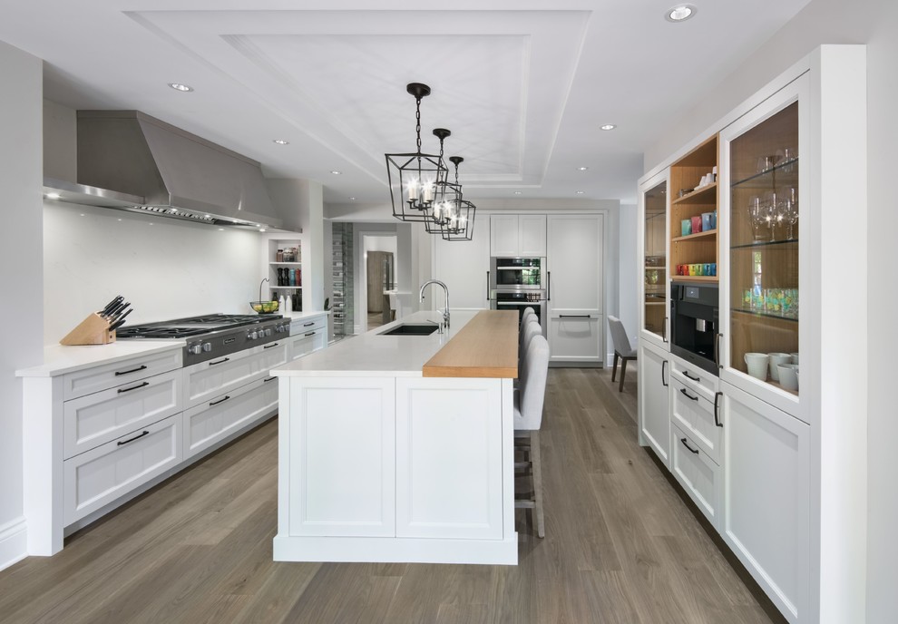 This is an example of a transitional separate kitchen in Ottawa with an undermount sink, shaker cabinets, white cabinets, white splashback, stainless steel appliances, medium hardwood floors, with island and white benchtop.