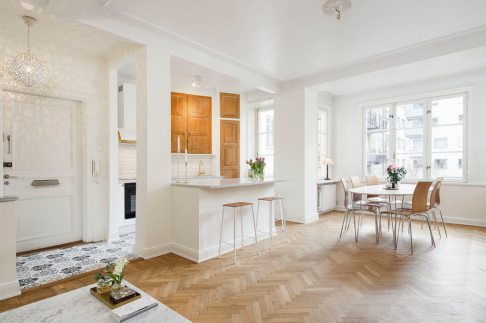 Inspiration for a mid-sized scandinavian single-wall open plan kitchen in Stockholm with raised-panel cabinets, medium wood cabinets, white splashback, subway tile splashback, light hardwood floors, with island, marble benchtops and black appliances.