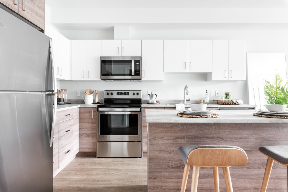 Design ideas for a small contemporary l-shaped kitchen in Vancouver with a double-bowl sink, flat-panel cabinets, light wood cabinets, laminate benchtops, stainless steel appliances, vinyl floors, with island and grey benchtop.