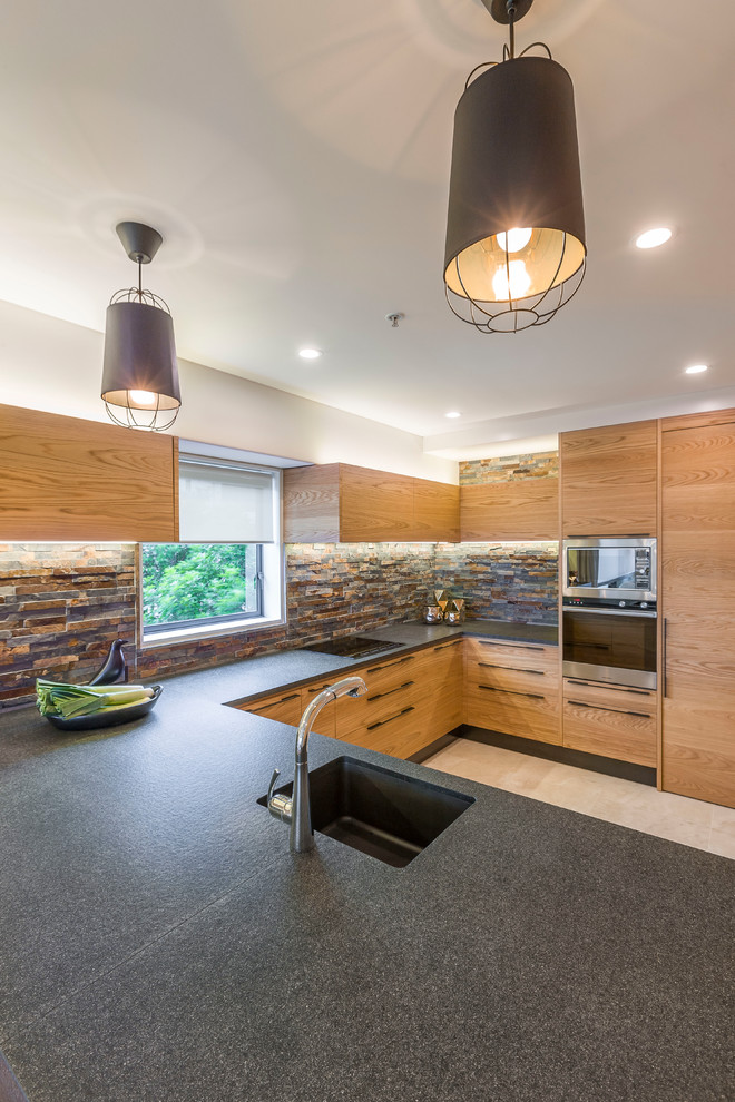 Mid-sized scandinavian u-shaped eat-in kitchen in Auckland with an undermount sink, flat-panel cabinets, light wood cabinets, granite benchtops, beige splashback, black appliances, light hardwood floors, with island and beige floor.