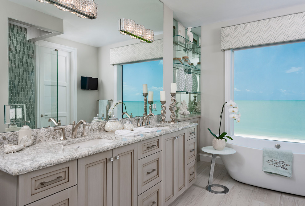 This is an example of a beach style bathroom in Other with recessed-panel cabinets, grey cabinets, a freestanding tub, grey walls, an undermount sink, grey floor and grey benchtops.