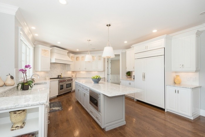 Large transitional u-shaped medium tone wood floor eat-in kitchen photo in Boston with an undermount sink, raised-panel cabinets, white cabinets, marble countertops, white backsplash, white appliances and an island