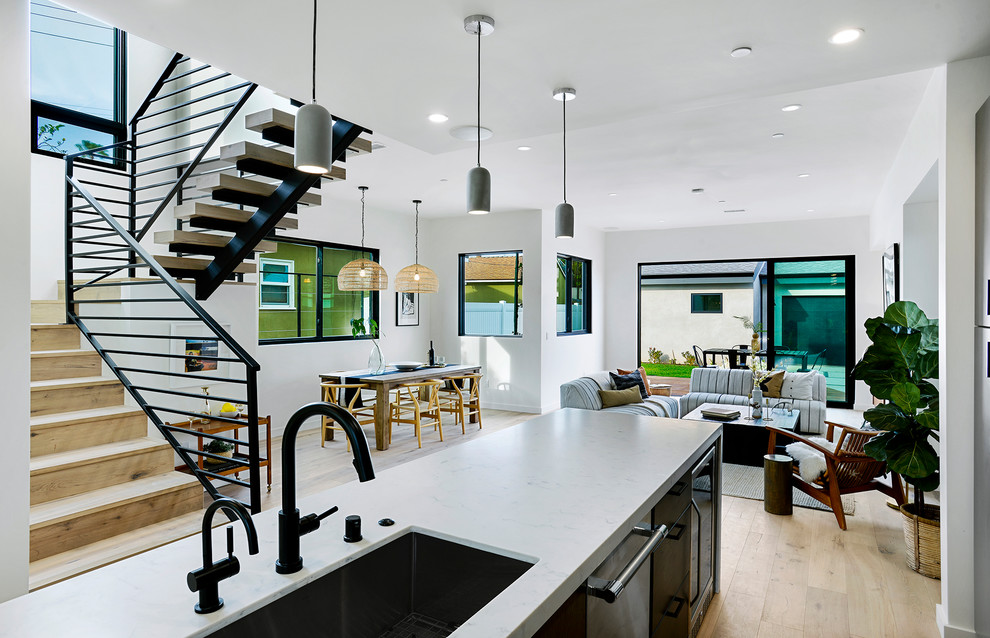 Expansive eclectic kitchen in Los Angeles with a double-bowl sink, flat-panel cabinets, dark wood cabinets, quartz benchtops, white splashback, porcelain splashback, stainless steel appliances, light hardwood floors, with island and white benchtop.