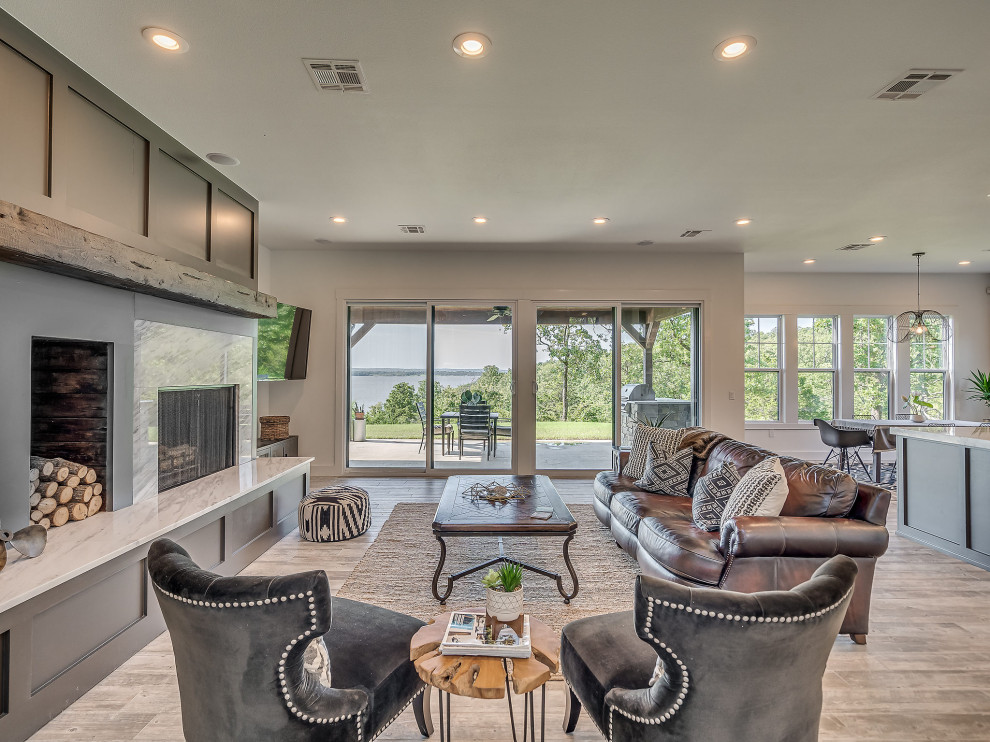 Large transitional open concept living room with white walls, ceramic floors, a standard fireplace, a stone fireplace surround, a corner tv and grey floor.