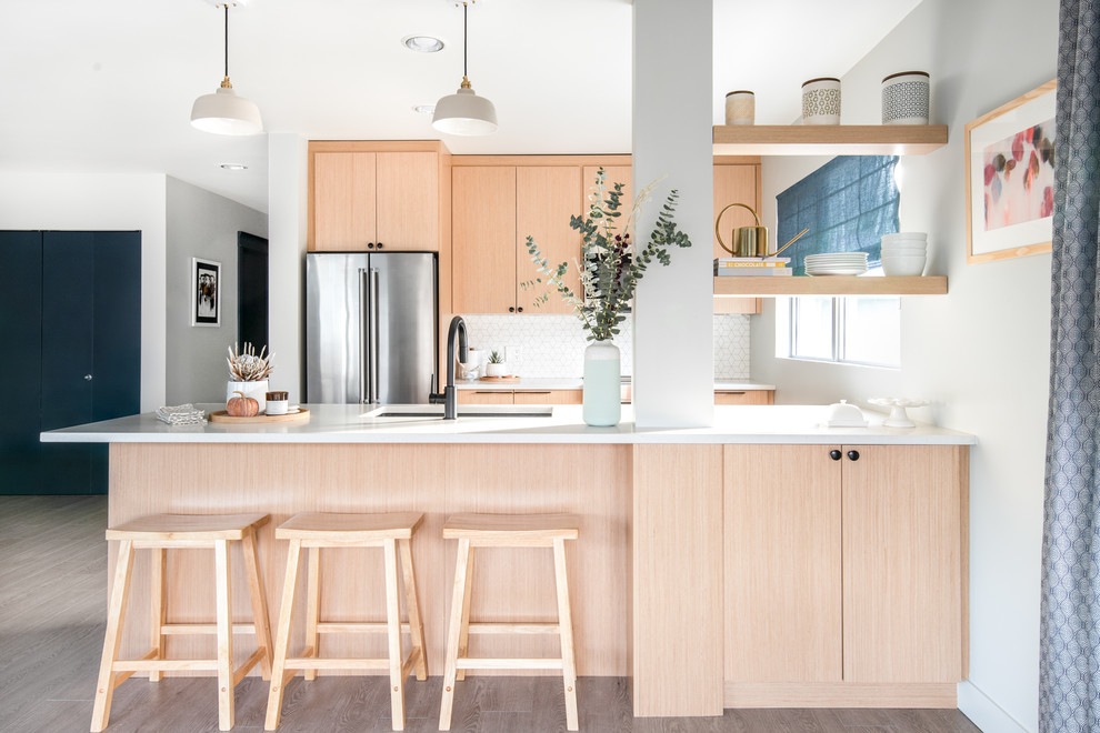 This is an example of a transitional galley kitchen in Vancouver with an undermount sink, flat-panel cabinets, light wood cabinets, white splashback, stainless steel appliances, light hardwood floors, beige floor and white benchtop.