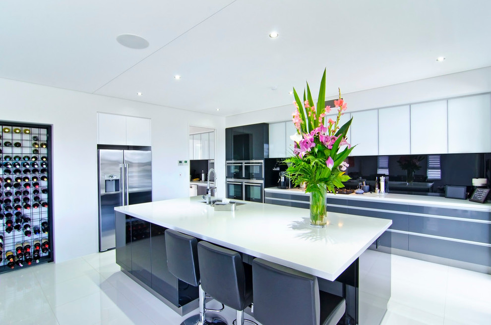 This is an example of a mid-sized contemporary l-shaped open plan kitchen in Gold Coast - Tweed with flat-panel cabinets, white cabinets, black splashback, glass sheet splashback, stainless steel appliances, an undermount sink and with island.
