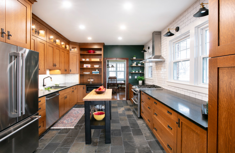 Design ideas for a small arts and crafts galley eat-in kitchen in St Louis with an undermount sink, recessed-panel cabinets, medium wood cabinets, soapstone benchtops, white splashback, subway tile splashback, stainless steel appliances, slate floors, with island, grey floor and black benchtop.