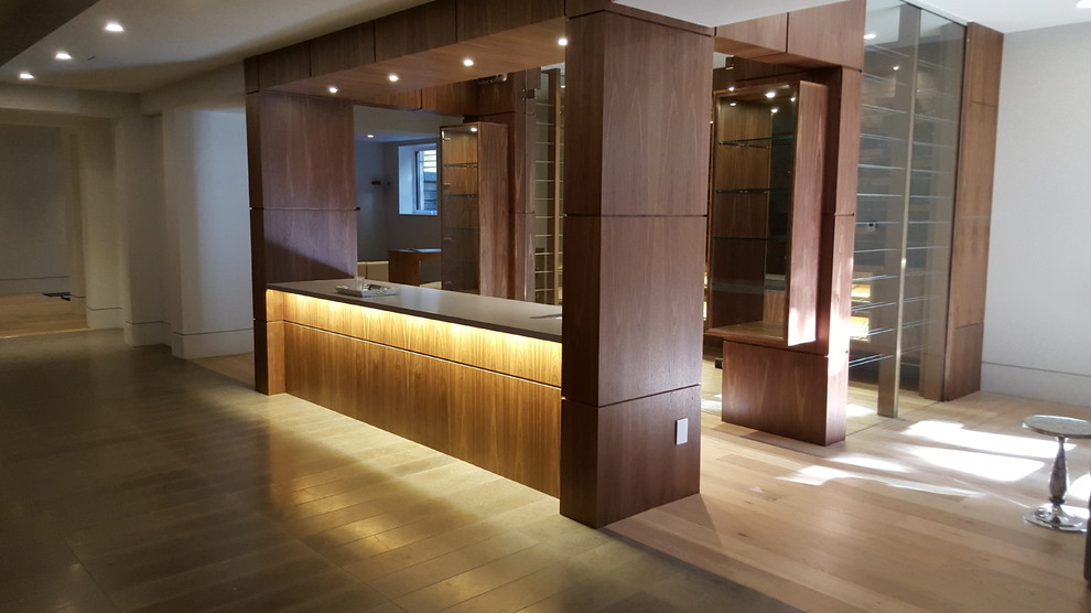 This is an example of a large contemporary l-shaped seated home bar in Toronto with medium wood cabinets, an undermount sink, flat-panel cabinets, marble benchtops, light hardwood floors and beige floor.