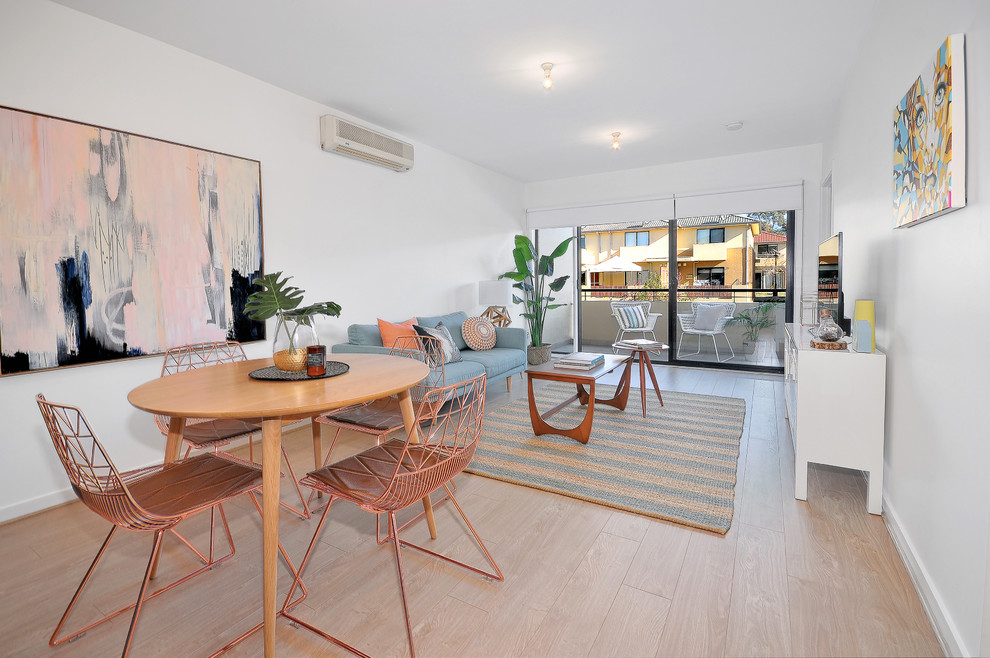 This is an example of a tropical open plan dining in Melbourne with white walls and light hardwood floors.
