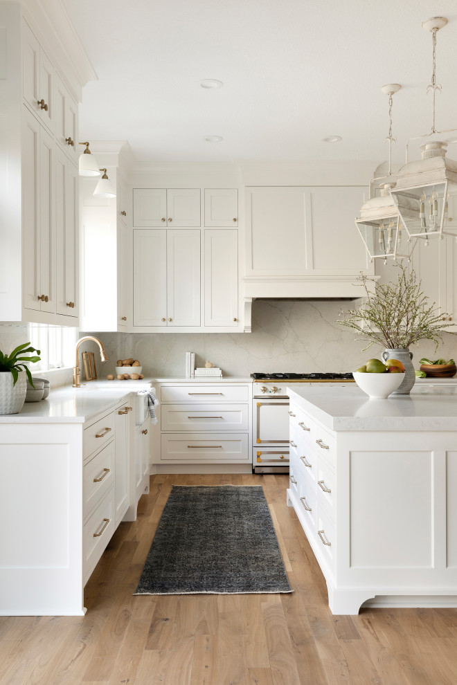 This is an example of a large transitional l-shaped eat-in kitchen in Minneapolis with a farmhouse sink, beaded inset cabinets, white cabinets, quartzite benchtops, white splashback, engineered quartz splashback, panelled appliances, light hardwood floors, with island, brown floor and white benchtop.