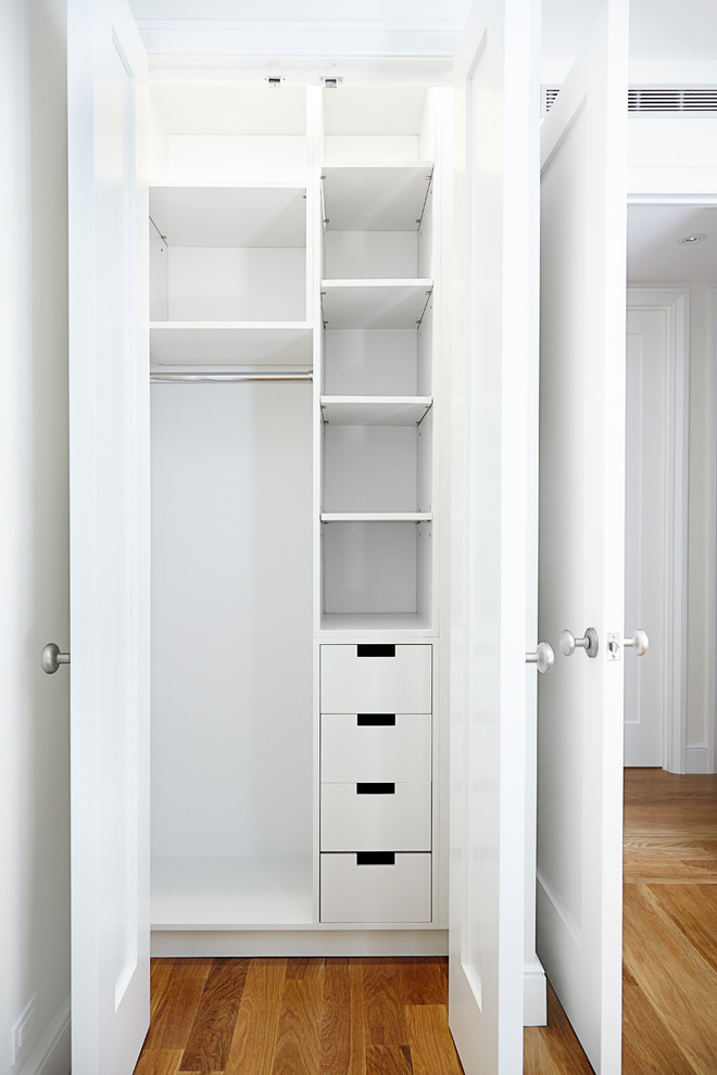 Design ideas for a small contemporary gender-neutral built-in wardrobe in New York with flat-panel cabinets, white cabinets and light hardwood floors.
