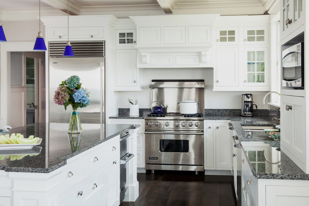 This is an example of a beach style kitchen in Boston with an undermount sink, shaker cabinets, white cabinets, stainless steel appliances, dark hardwood floors and with island.