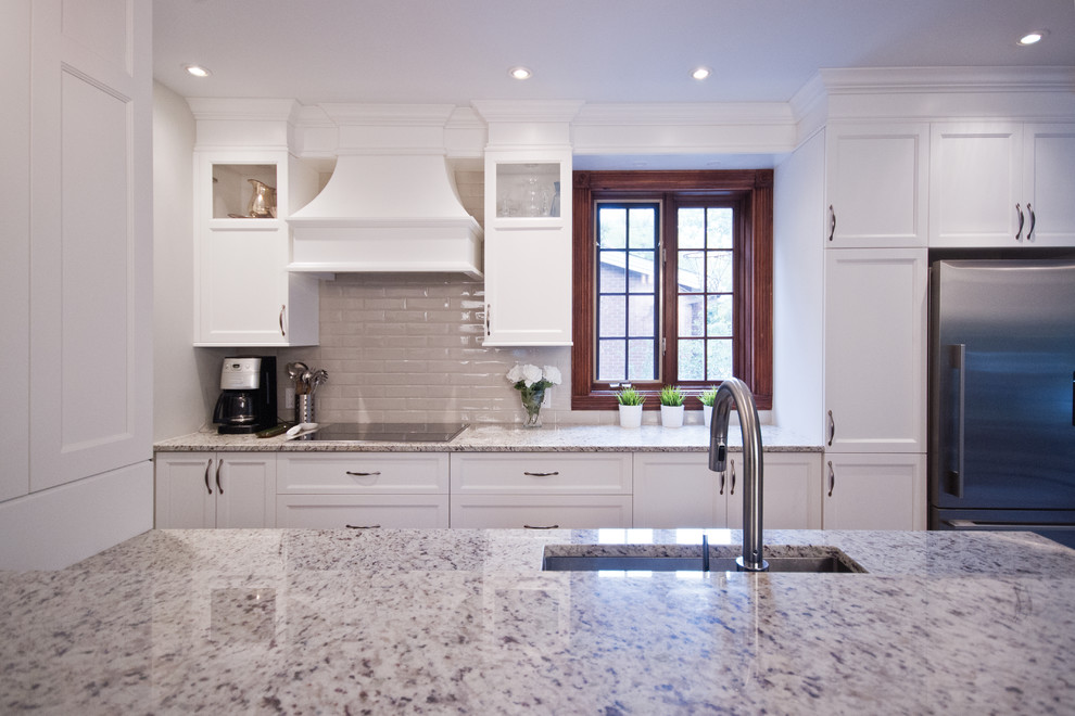 Eat-in kitchen - mid-sized transitional galley ceramic tile eat-in kitchen idea in Montreal with an undermount sink, shaker cabinets, white cabinets, granite countertops, beige backsplash, subway tile backsplash, stainless steel appliances and an island