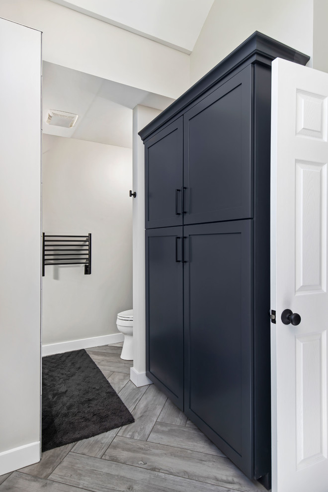 Photo of a large contemporary master bathroom in Detroit with shaker cabinets, blue cabinets, a freestanding tub, an alcove shower, a two-piece toilet, gray tile, porcelain tile, grey walls, porcelain floors, an undermount sink, engineered quartz benchtops, grey floor, a hinged shower door and white benchtops.