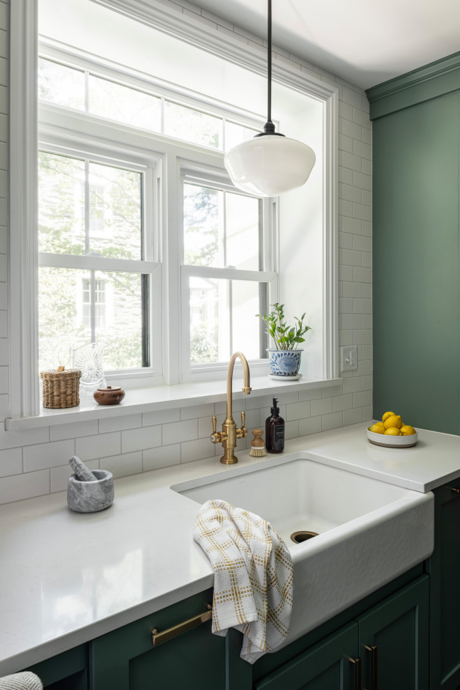 Design ideas for a mid-sized transitional galley separate kitchen in Philadelphia with a farmhouse sink, shaker cabinets, green cabinets, quartz benchtops, white splashback, subway tile splashback, stainless steel appliances, porcelain floors, grey floor and white benchtop.