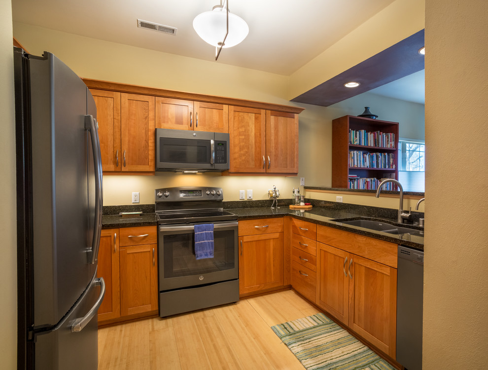 Mid-sized transitional u-shaped light wood floor open concept kitchen photo with an undermount sink, shaker cabinets, medium tone wood cabinets, granite countertops, black appliances, no island and black countertops