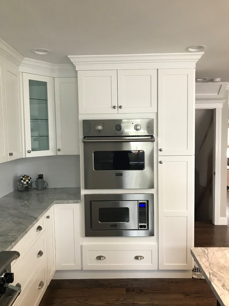 Mid-sized transitional u-shaped dark wood floor and brown floor eat-in kitchen photo in New York with a farmhouse sink, recessed-panel cabinets, white cabinets, wood countertops, white backsplash, limestone backsplash, stainless steel appliances, an island and white countertops