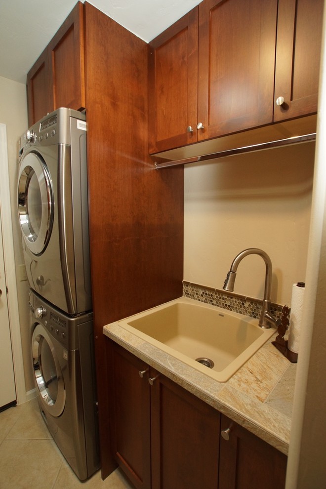 Small single-wall laundry room in Phoenix with a drop-in sink, shaker cabinets, tile benchtops, beige walls, porcelain floors, a stacked washer and dryer, beige floor and dark wood cabinets.