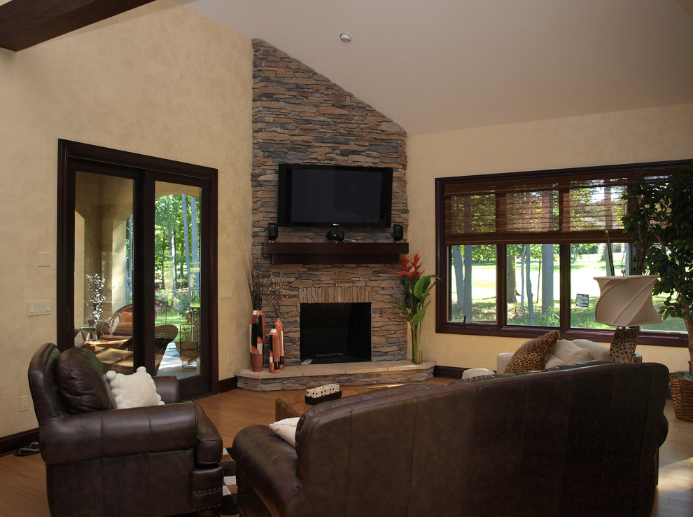 This is an example of a large arts and crafts open concept living room in Cleveland with beige walls, medium hardwood floors, a standard fireplace, a stone fireplace surround and a wall-mounted tv.