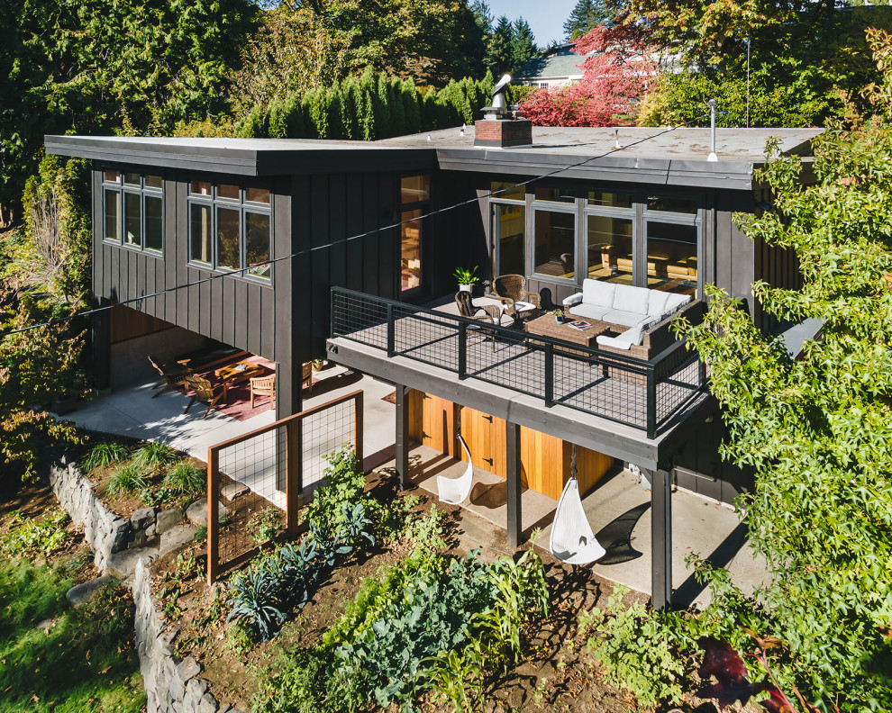 This is an example of a large midcentury two-storey black house exterior in Portland with wood siding, a butterfly roof and board and batten siding.