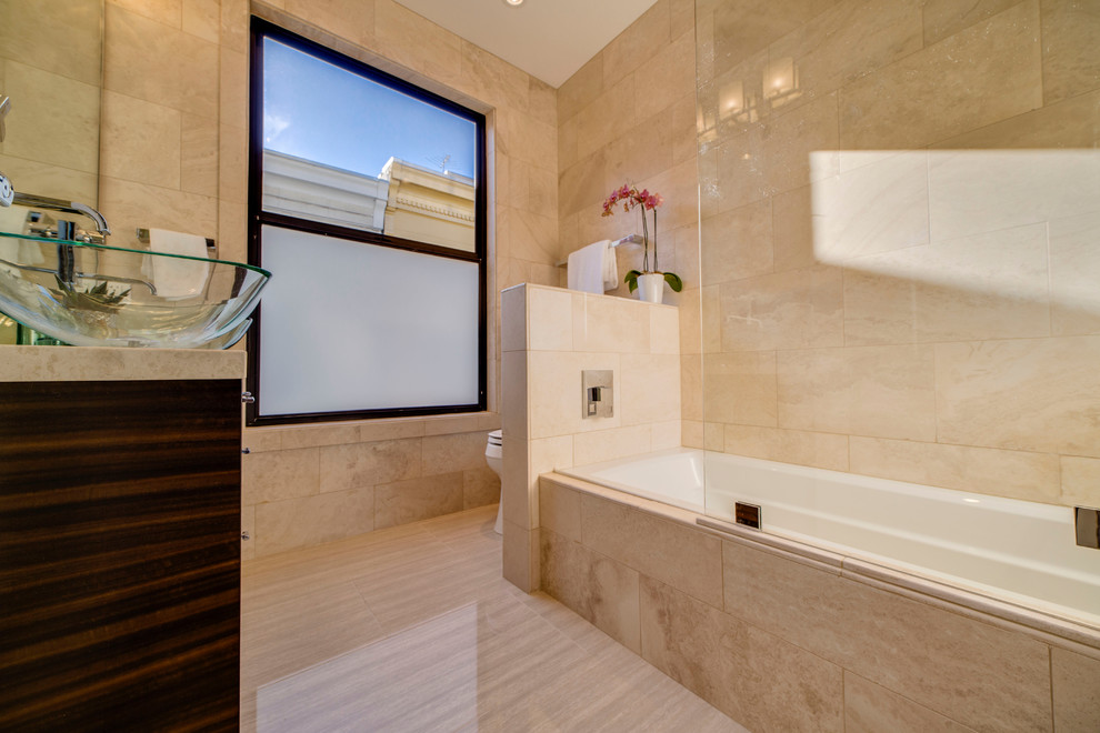 Large contemporary master bathroom in San Francisco with a vessel sink, glass-front cabinets, dark wood cabinets, marble benchtops, a drop-in tub, a shower/bathtub combo, a one-piece toilet, beige tile, porcelain tile, beige walls and light hardwood floors.