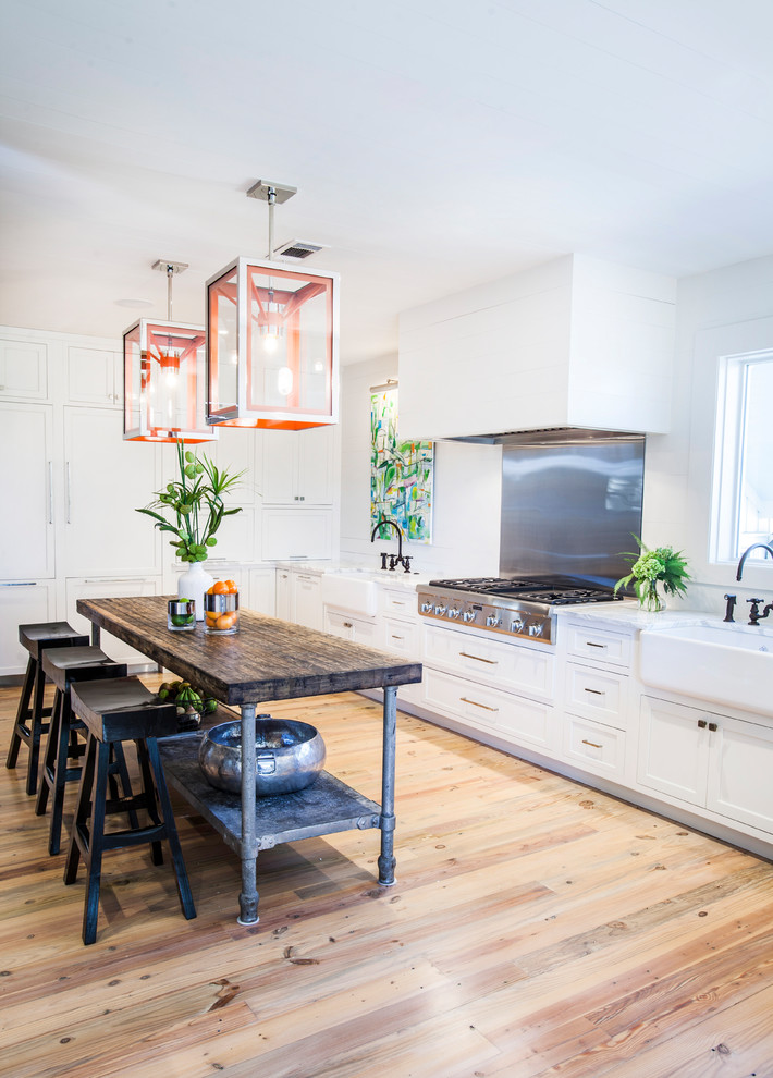 Beach style kitchen in Atlanta with a farmhouse sink, shaker cabinets, white cabinets, metallic splashback, stainless steel appliances, light hardwood floors, with island and white benchtop.