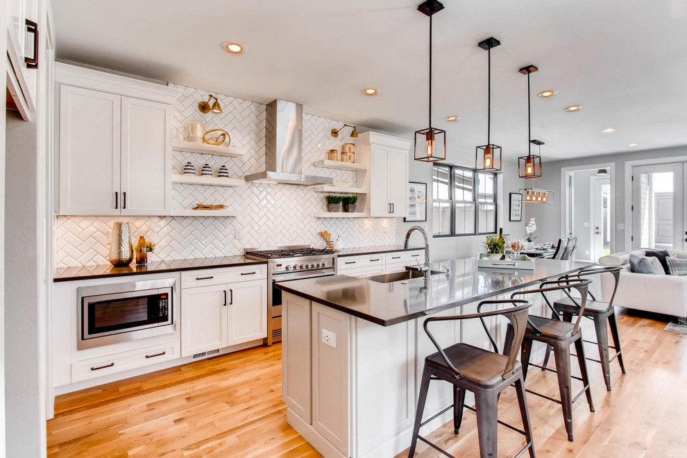 Design ideas for a country galley open plan kitchen in Denver with a farmhouse sink, shaker cabinets, white cabinets, white splashback, subway tile splashback, medium hardwood floors, with island, brown floor and black benchtop.