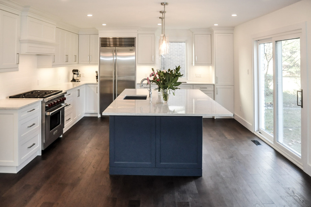 Inspiration for a large transitional l-shaped dark wood floor and brown floor open concept kitchen remodel with an undermount sink, shaker cabinets, white cabinets, quartzite countertops, white backsplash, ceramic backsplash, stainless steel appliances and an island