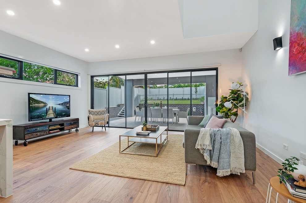 This is an example of a contemporary open concept living room in Sydney with white walls, medium hardwood floors, a freestanding tv and brown floor.
