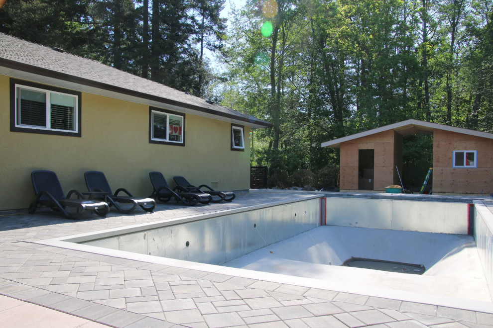 Ejemplo de piscina actual grande rectangular en patio trasero con adoquines de hormigón