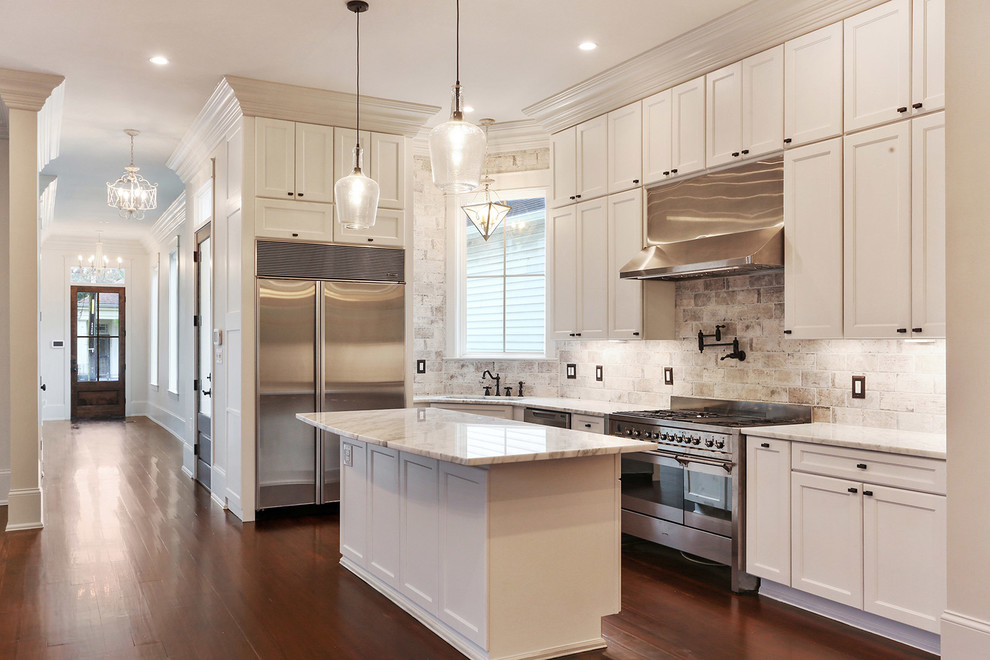 Mid-sized transitional l-shaped kitchen in New Orleans with an undermount sink, recessed-panel cabinets, white cabinets, marble benchtops, beige splashback, brick splashback, stainless steel appliances, dark hardwood floors and with island.