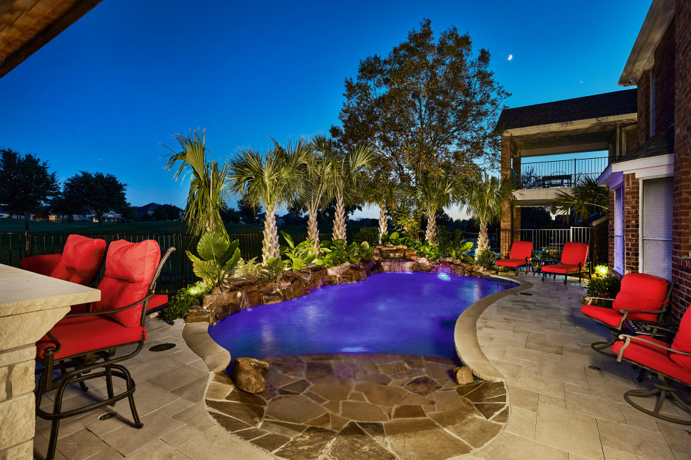 Photo of a mid-sized tropical backyard custom-shaped pool in Dallas with with a pool and natural stone pavers.