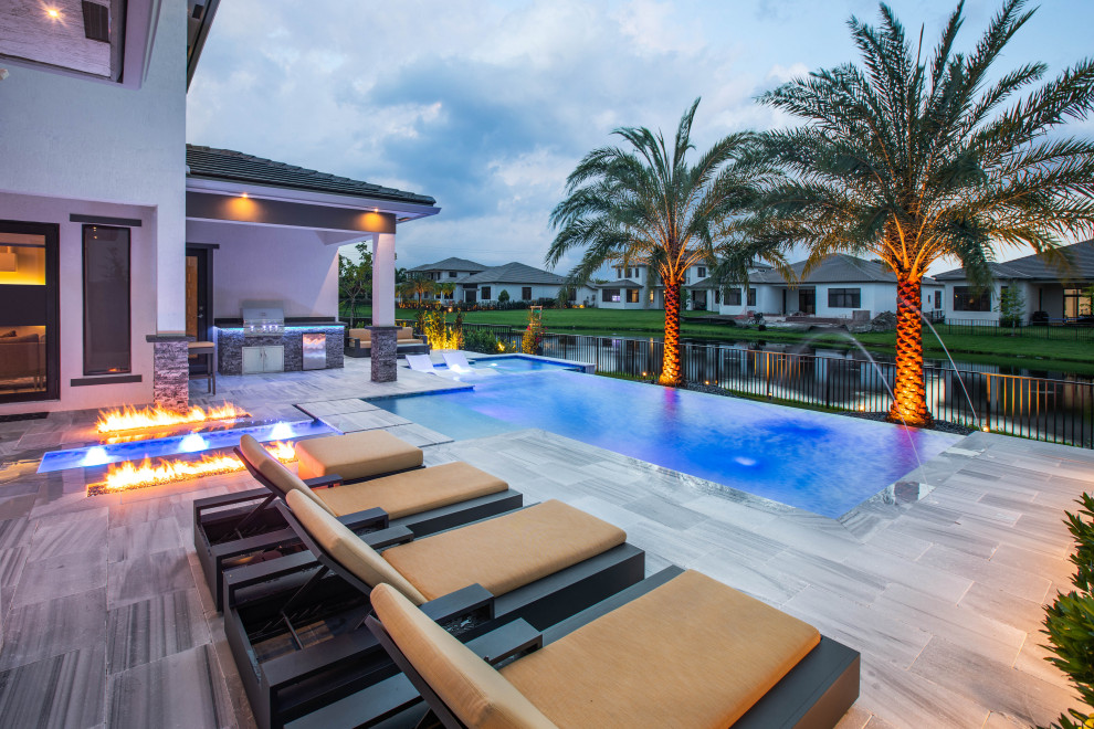 Photo of a large modern backyard custom-shaped infinity pool in Miami with with a pool and natural stone pavers.