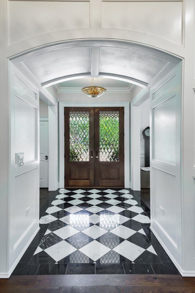 На фото: фойе среднего размера в классическом стиле с белыми стенами, мраморным полом, двустворчатой входной дверью, входной дверью из темного дерева, белым полом и панелями на части стены